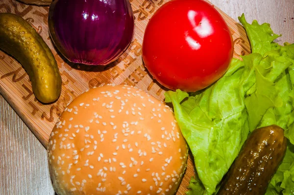 Kırmızı domates, mor soğan, yeşil salata, salatalık turşusu ve ahşap arka plan üzerinde topuz.