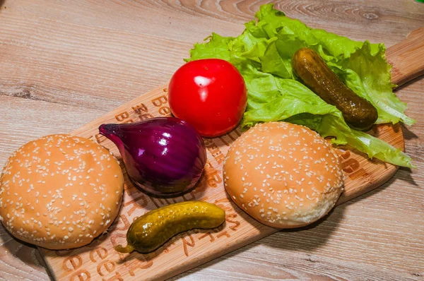 Kırmızı domates, mor soğan, yeşil salata, salatalık turşusu ve ahşap arka plan üzerinde topuz.