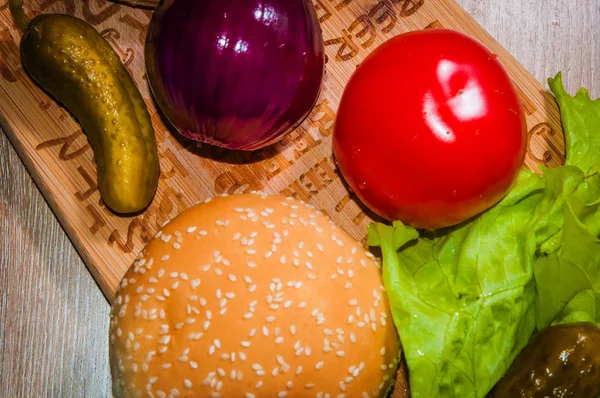Kırmızı domates, mor soğan, yeşil salata, salatalık turşusu ve ahşap arka plan üzerinde topuz.