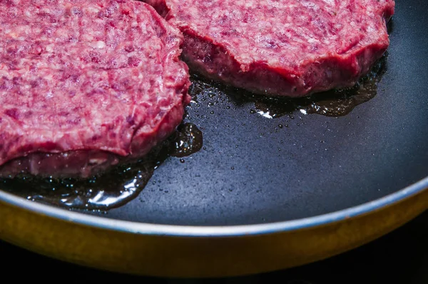 Panelde kızaran hamburger pirzolası. Mutfakta pişen ekmek parçaları. Yağlı ve yağlı bir hamburgerin dumanıyla pişirilen burger sandviçi. Kalemlerin üzerindeki peynir.