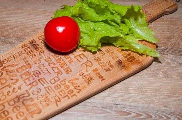 Yeşil salata ve mutfak masası ve ahşap arka plan üzerinde kırmızı domates.