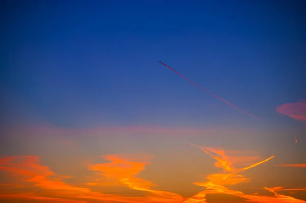 Orange clouds with aircraft trails sky background and city light midnight evening time — Stock Photo, Image