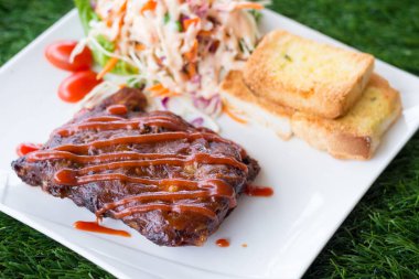 Sarımsaklı ekmek ve sebze salatası ile servis barbekü soslu domuz barbekü kaburga yakından görünümü.