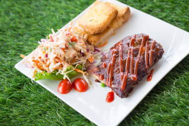 Sarımsaklı ekmek ve sebze salatası ile servis barbekü soslu domuz barbekü kaburga yakından görünümü.