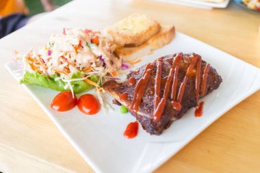 Sarımsaklı ekmek ve sebze salatası ile servis barbekü soslu domuz barbekü kaburga yakından görünümü.