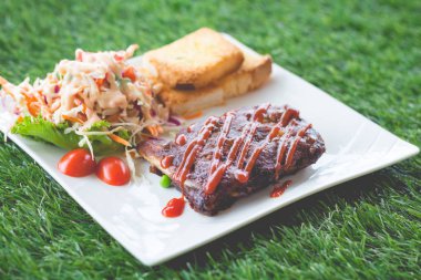 Sarımsaklı ekmek ve sebze salatası ile servis barbekü soslu domuz barbekü kaburga yakından görünümü.