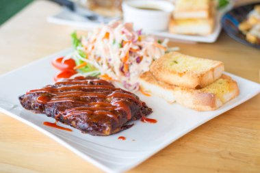 Sarımsaklı ekmek ve sebze salatası ile servis barbekü soslu domuz barbekü kaburga yakından görünümü.