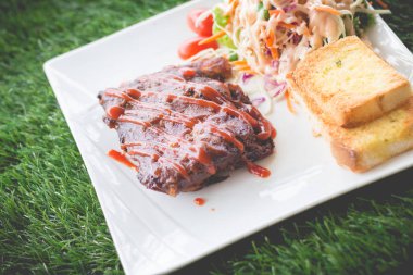 Sarımsaklı ekmek ve sebze salatası ile servis barbekü soslu domuz barbekü kaburga yakından görünümü.