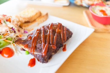 Sarımsaklı ekmek ve sebze salatası ile servis barbekü soslu domuz barbekü kaburga yakından görünümü.