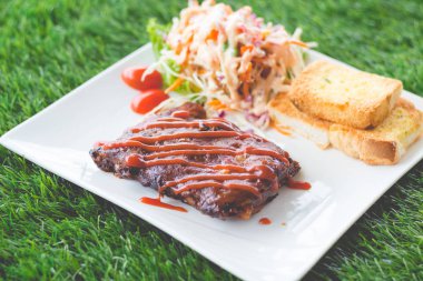 Sarımsaklı ekmek ve sebze salatası ile servis barbekü soslu domuz barbekü kaburga yakından görünümü.