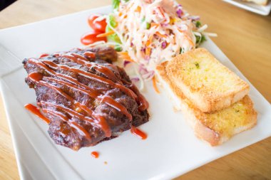 Sarımsaklı ekmek ve sebze salatası ile servis barbekü soslu domuz barbekü kaburga yakından görünümü.