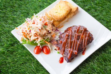 Sarımsaklı ekmek ve sebze salatası ile servis barbekü soslu domuz barbekü kaburga yakından görünümü.