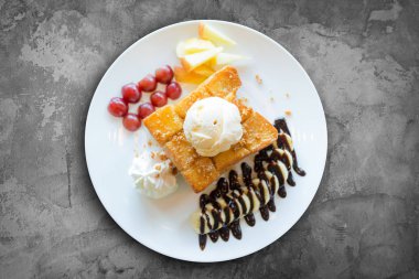 Vanilyalı dondurma, krem şanti ve çikolata şurubu ile bal tost. Muz, üzüm ve elma ile servis edilir (seçici odak)