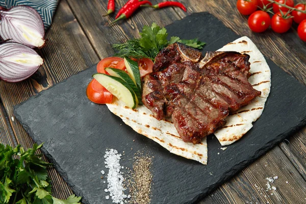 Biberiye, tuz ve biber siyah taş plaka üzerinde ızgara sığır eti biftek. Izgara striploin biftek dilimlenmiş. Biberiye taze yaz barbekü ile terbiyeli sulu kalın ızgara sığır eti biftek.