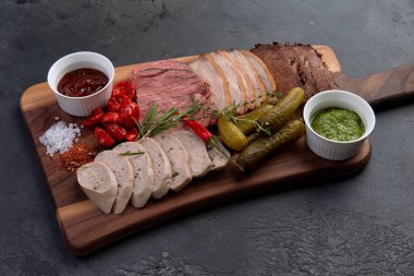 Lezzetli meze çeşitleri, salatalık turşusu, güneşte kurutulmuş domates ve iki soslu siyah tahta üzerinde.