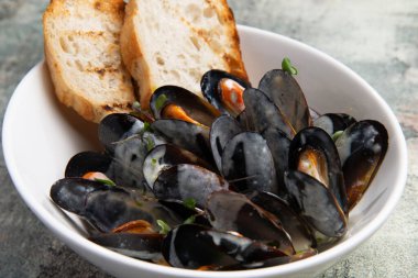 Yemek için hazır midyeler, gri arka planda bir tabakta tost.