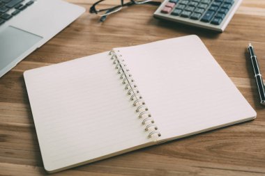 Çalışma masası sabah ışık ile defter ve kalem, hesap makinesi, Gözlük, dizüstü bilgisayar ile. Seçilen odak.