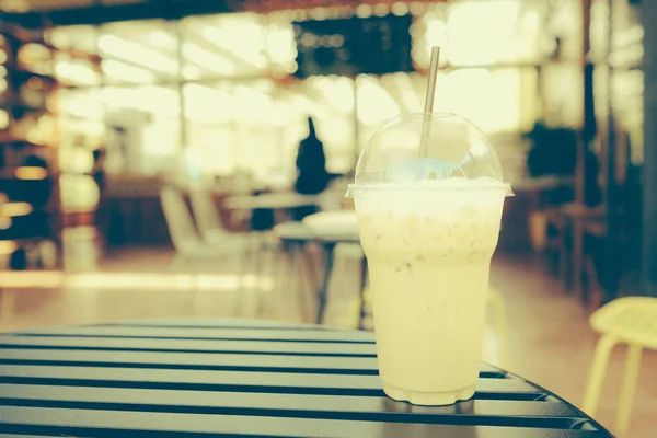 Iced  coffee cappuccino in takeaway cup on the wooden tabletop in the coffee shop.