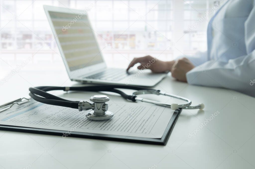 Stethoscope on medical document and doctor working with laptop computer with  hospital background. 