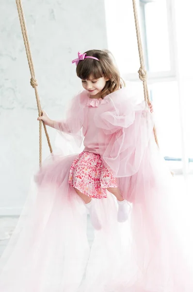 Милая Маленькая Девочка Розовой Одежде Луком Волосах Качелях Помещении — стоковое фото