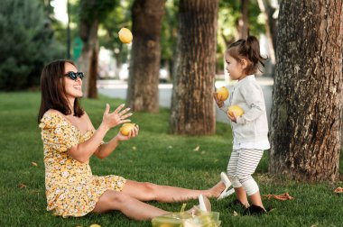 Şık anne par çim üzerinde oturan kızının önünde limon hokkabazlık