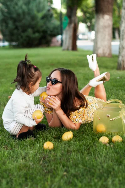 Funny mum with the daughter play with lemons lying on a grass in par