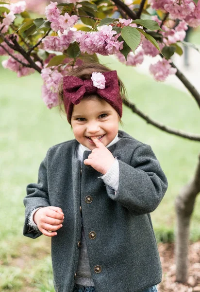 一个可爱的小女孩的肖像 在她的头上的蝴蝶结在盛开的萨库尔公园 — 图库照片