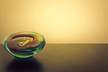 Koyu ahşap bir masada sarı arka planı olan renkli camdan yapılmış küçük bir kül tablası.