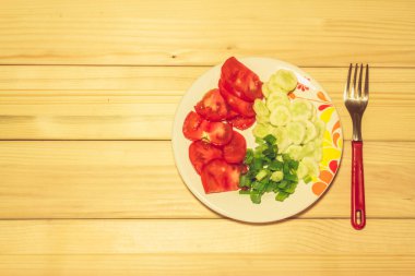 Dilimlenmiş birkaç sebze, bir çatalın yanında, ahşap arka planda.