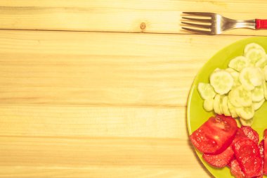 Tahta arka planı olan bir çatalın yanındaki tabakta birkaç sebzeye yakın çekim yap.