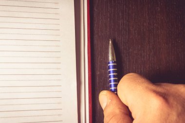 Ahşap bir arka planda gündemin yanında kalem tutan bir ele yakın çekim.