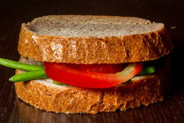 Birkaç yeşil soğan yaprağı ve ahşap zemin üzerinde bir dilim domatesle yapılan basit bir sandviçe yakın çekim.