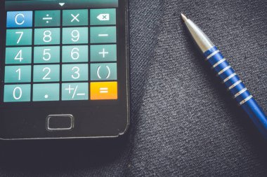 Metalik mavi bir kalem ve iş ceketinde bir telefonla takım elbise dokusunun yakın çekimi.