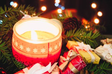 Noel arkaplanı, çam ağacı dalları, hediyeler, kırmızı mum ve mavi ve sarı ışıklı çam kozalakları. Renkli mücevherler, mavi tatil süslemeleri.