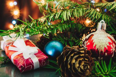 Noel arkaplanı, çam ağacı dalları, hediyeler ve mavi ve sarı ışıklı çam kozalakları. Renkli mücevherler, mavi tatil süslemeleri.