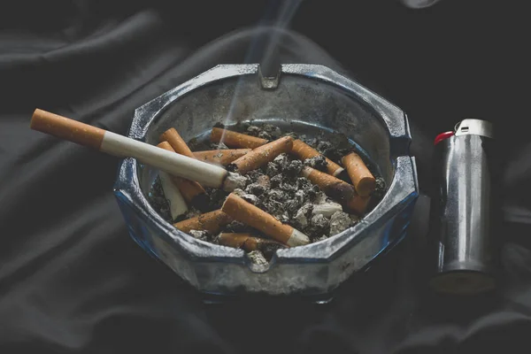 Cigarettacsikkek Hamutartóban Még Mindig Égő Cigarettával Sötét Gyűrött Selyem Háttéren — Stock Fotó