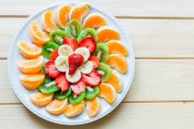 Tabak portakal dilimleri, kivi, muz dilimleri ve ahşap masa üzerindeki çileklerle süslenmiş.