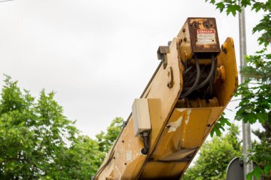 Yeşil yaprakların yanında üzerinde tehlike işareti olan bir servis aracı vinci.