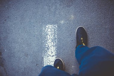 Siyah spor ayakkabılı bir adam yolun ortasında yürüyor. Asfalt dokusu. Polyester kumaş.