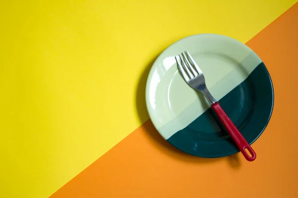 boş yeşil plato ve turuncu ve sarı arka planda kırmızı çatal