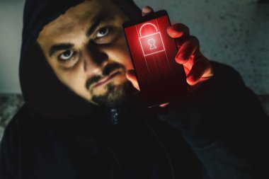 Elinde siyah ekranlı bir telefon tutan öfkeli bir hacker. Siber saldırı uyarısı. Fidye yazılımı kavramı