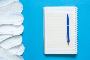Beyaz kadınlar bir defter ve mavi arka planda bir kalem yanında soğururlar..