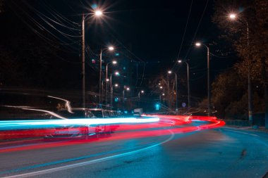 Gece vakti sokak lambaları ve arabaların ardında renkli parlak farlar bırakan şehir.