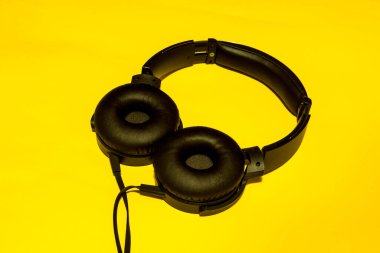 Tek bir siyah kulaklık, kalın bir kablo ve büyük bir kulaklık, sarı bir arka plan.