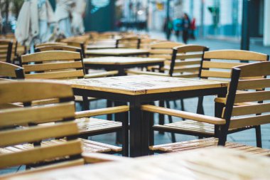 Küçük boş teras, içinde kimse yok ahşap sandalye ve masalar, yağmurlu bir günde şehrin kaldırımında sıradan bir yer.