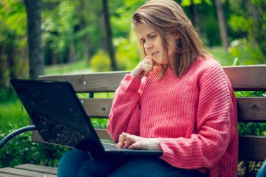 Pembe bluz giyen genç bir kadın dizüstü bilgisayara bakıyor ve hayal kuruyor. Bir bankta oturmuş bilgisayar öğrencisi bir kadını kullanıyor.