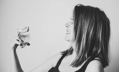 Gülümseyen genç bir kadın boynundaki beyaz arka plana parfüm sıkıyor. Mutlu kız zarif bir görünüm için güzel bir koku almaya çalışıyor.