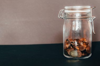 Kapalı cam kavanoz, plastik kapaklı ve metal kelepçe yarısı küçük sikkelerle dolu gri bir arka plan Tasarruf, yatırım, iyi zenginlik ve mali eğitim imajı