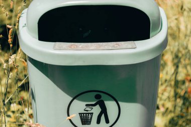 Parkta üzerinde geri dönüşüm işareti olan gri kirli plastik çöp kutusu. Şehirdeki çöp öğütme konteynırları. Atık toplamak ve çevreyi korumak için küçük çöp kutusu