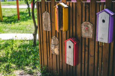 Parkta üzerinde renkli kuş evleri asılı parlak kahverengi ahşap çitler. Doğadaki doğal bir maddeden dekoratif duvar üzerine küçük oyuncak evler yapıştırılmış.